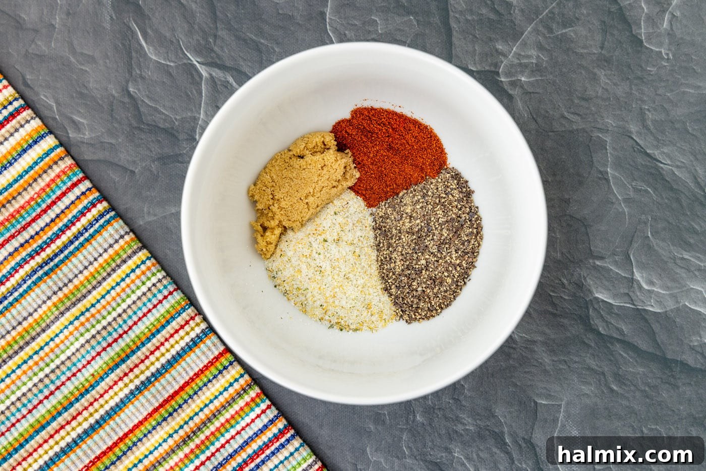A bowl filled with a perfectly mixed spice rub, featuring garlic salt, black pepper, brown sugar, and smoked paprika, ready to season the lamb chops.
