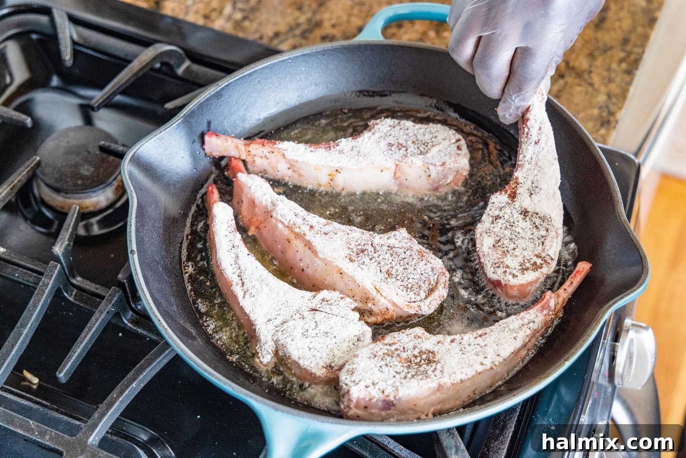 A lollipop lamb chop being gently placed into a hot, heavy-bottomed skillet with shimmering olive oil, ready for searing.