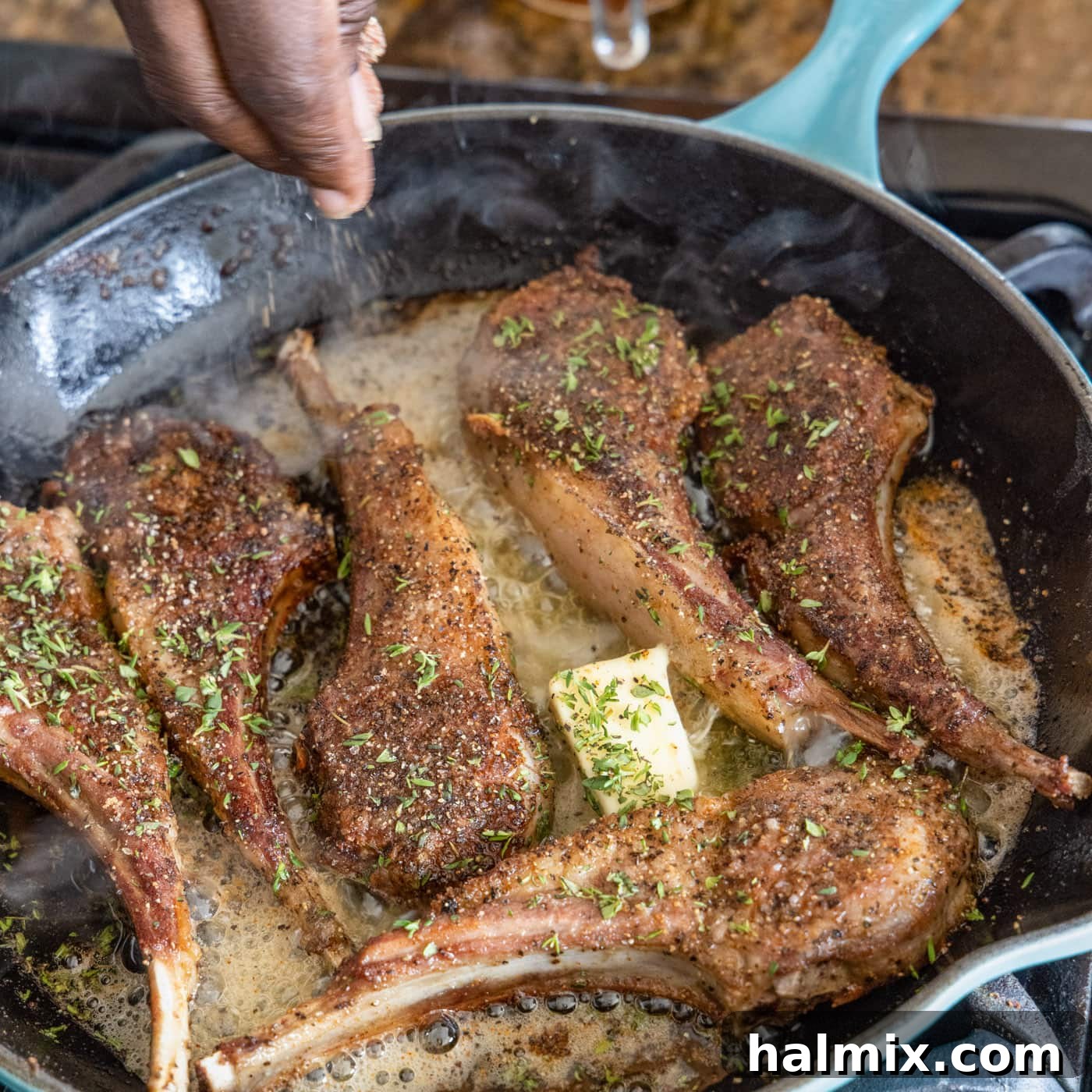 Sizzling lollipop lamb chops in a skillet, adorned with melting butter and freshly sprinkled thyme leaves, enhancing their aroma and flavor.