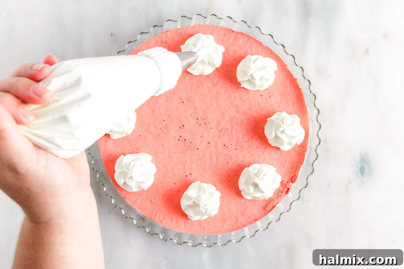 Decorating the top of the set layered jello pie with piped whipped cream swirls and festive sprinkles.