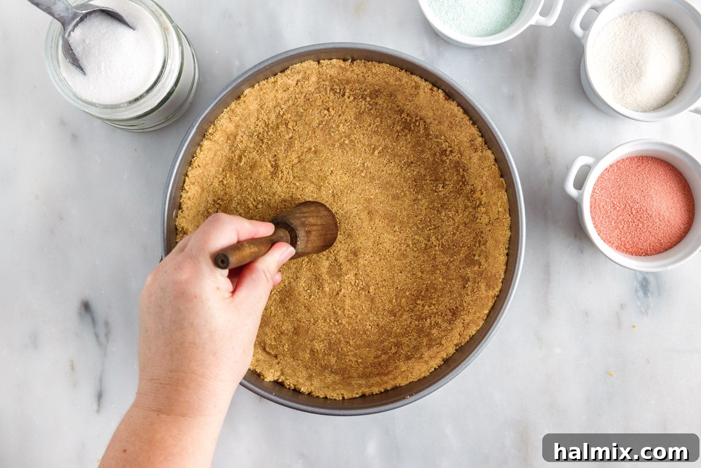 Pressing the graham cracker crumb mixture firmly into a springform pan to create an even pie crust.