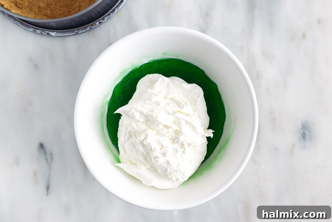 Adding Cool Whip to the slightly thickened lime jello mixture, preparing for whisking.