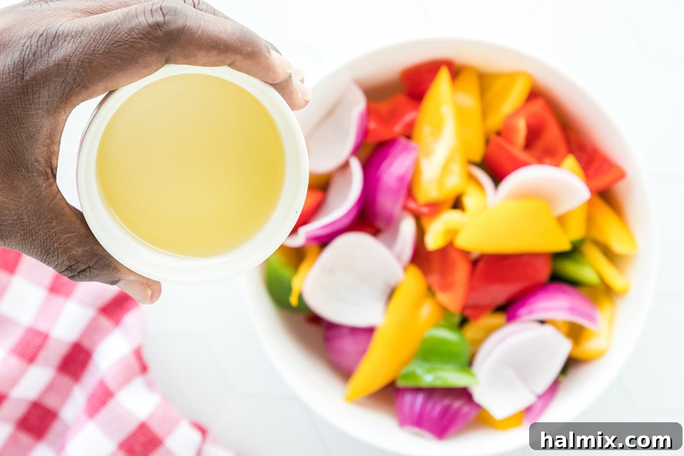 Freshly cut red onion and colorful bell peppers in a bowl, being tossed with olive oil to prepare them for stir-frying.