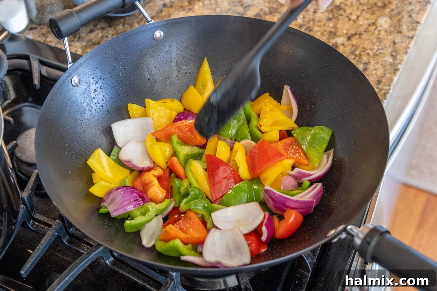 Colorful bell peppers and red onion being actively stir-fried in a hot wok, showing signs of browning and becoming tender-crisp.