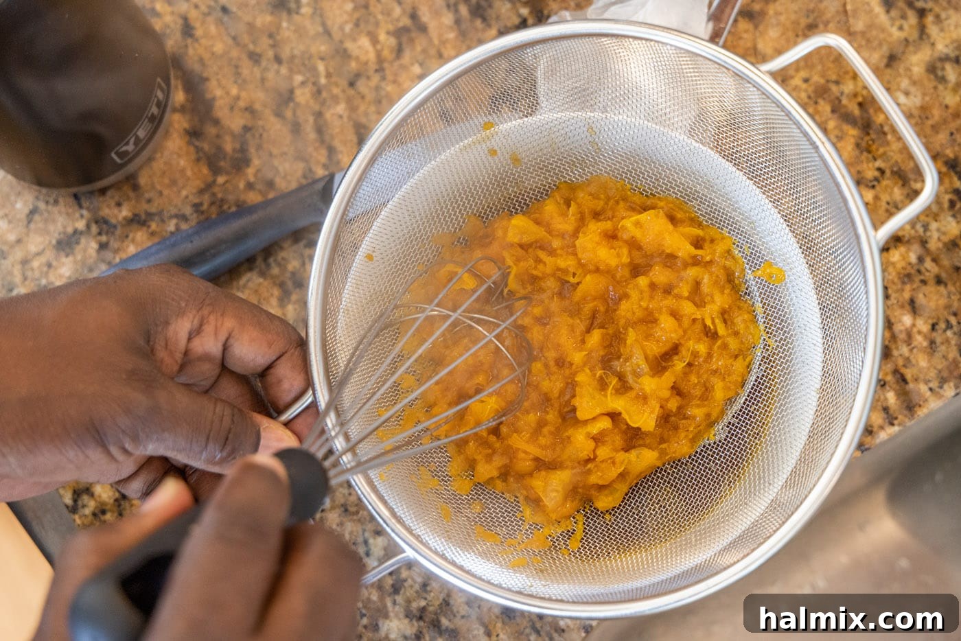 A hand using a fine mesh strainer to separate the whole clementines from the rich, aromatic sauce, ensuring a smooth finish for the dish.