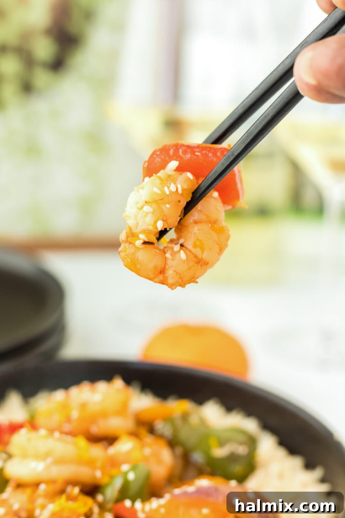 A close-up of a single shrimp from the Clementine Pepper Shrimp dish, perfectly glazed and being lifted by chopsticks, highlighting its succulence and flavor.
