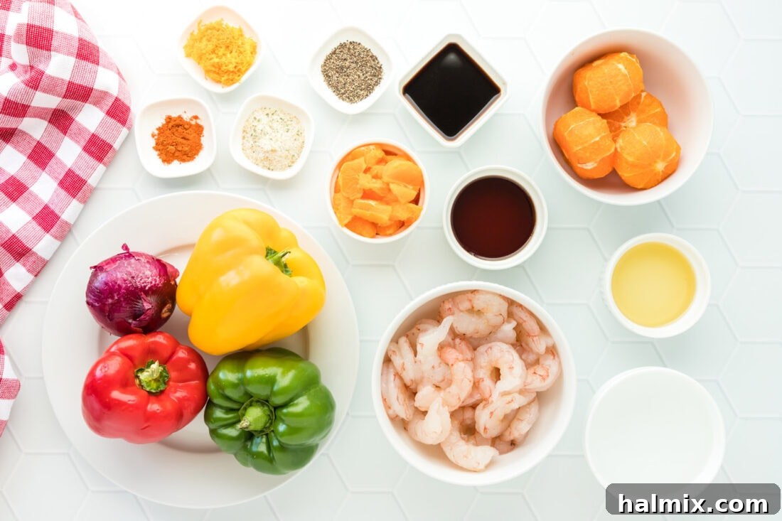 A selection of fresh ingredients neatly arranged, including clementines, colorful bell peppers, red onion, raw shrimp, olive oil, and spices, laid out for making Citrus Pepper Shrimp.
