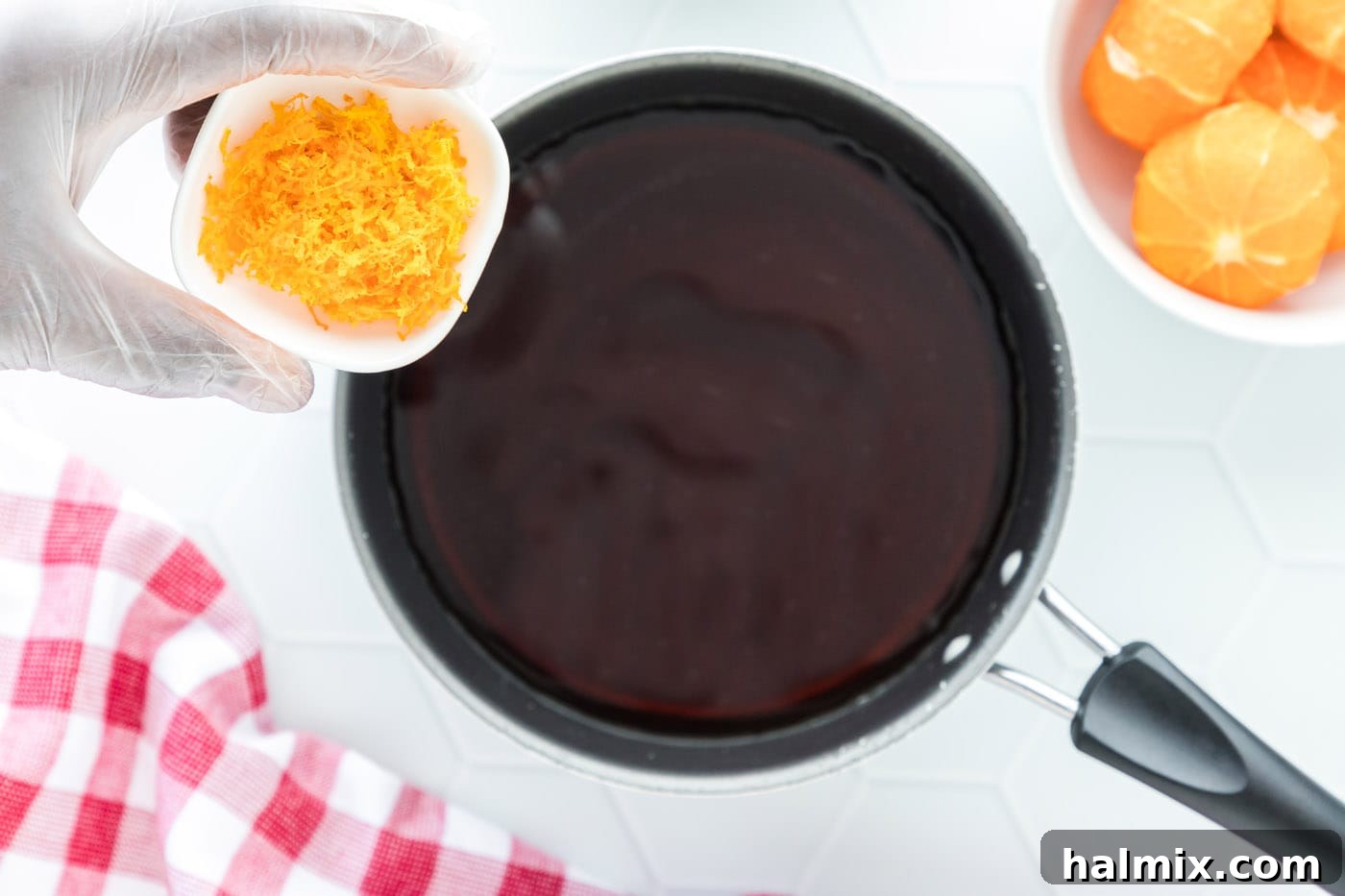 Hand grating clementine zest directly into a saucepan filled with soy sauce, maple syrup, and water, beginning the sauce preparation.