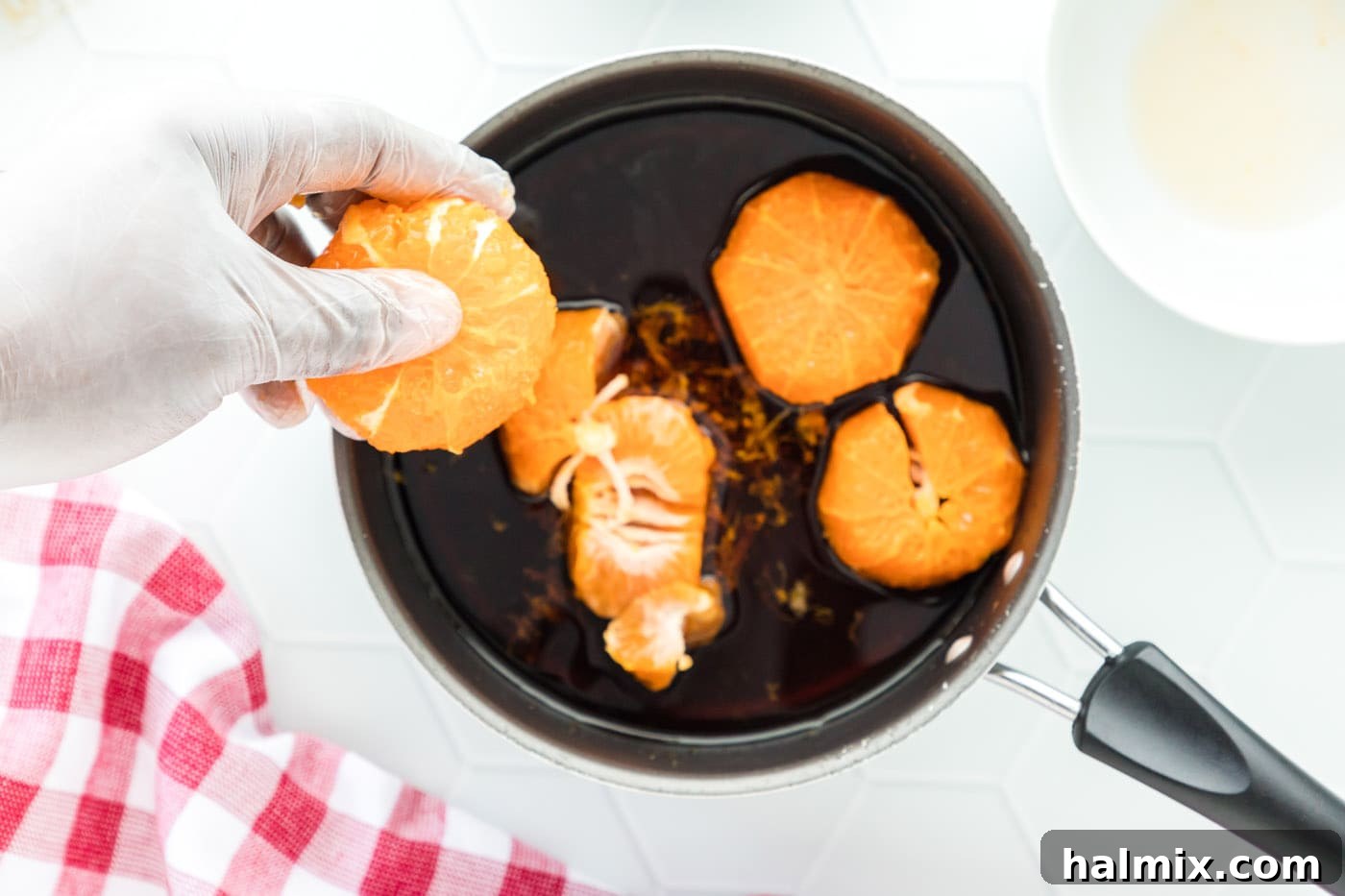 Four whole, peeled clementines gently placed into the simmering sauce in a pan, infusing it with their sweet citrus flavor.