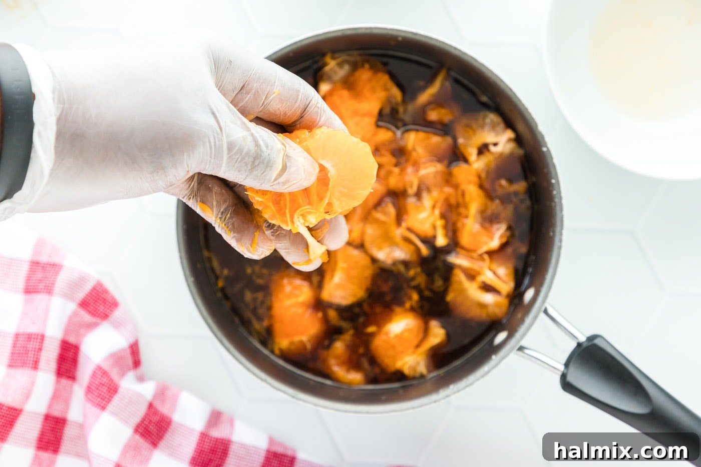 A close-up view of the clementine-infused sauce simmering gently in a saucepan, with the whole clementines releasing their flavors.