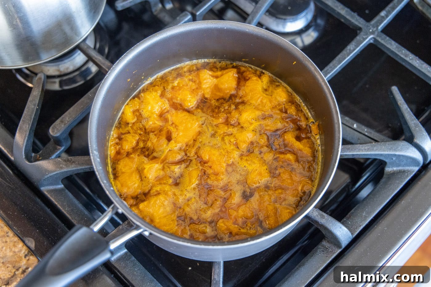 A rich, amber-colored clementine citrus pepper shrimp sauce bubbling gently in a saucepan, indicating it's been simmering and developing flavor.