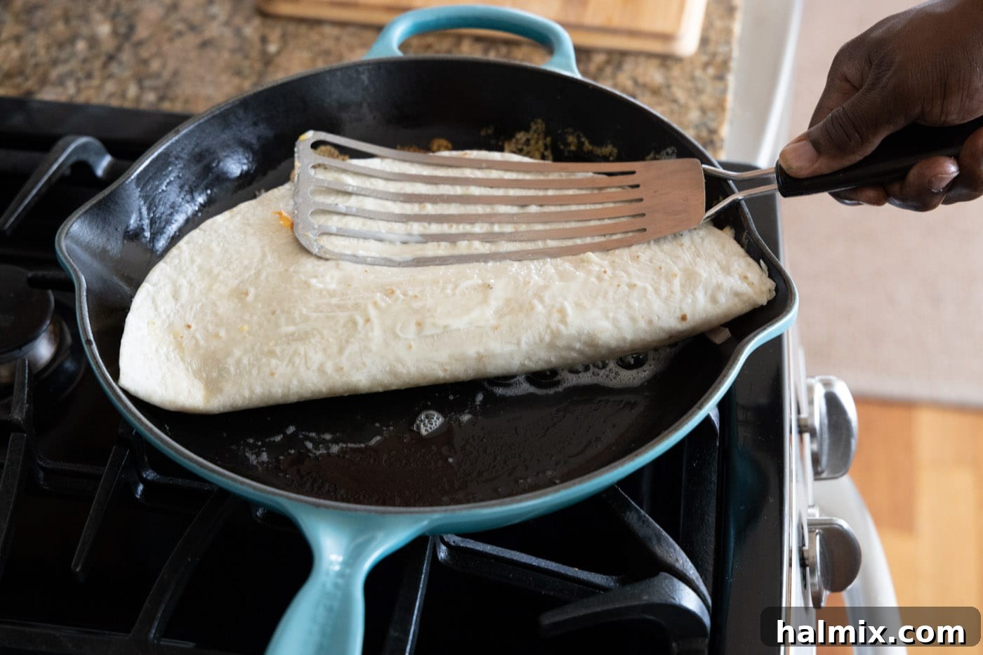 Pressing a chicken quesadilla into a hot skillet