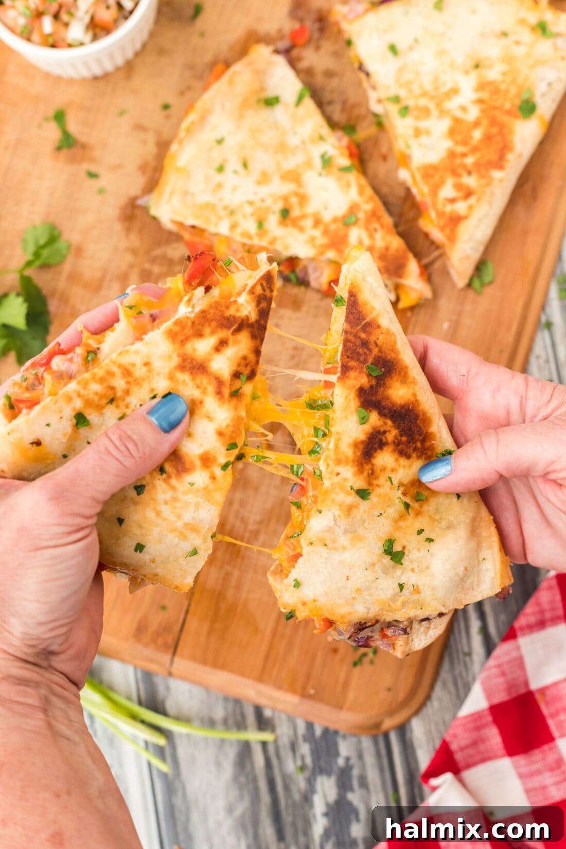 A hand pulling apart a chicken quesadilla to reveal the melted cheese and fillings