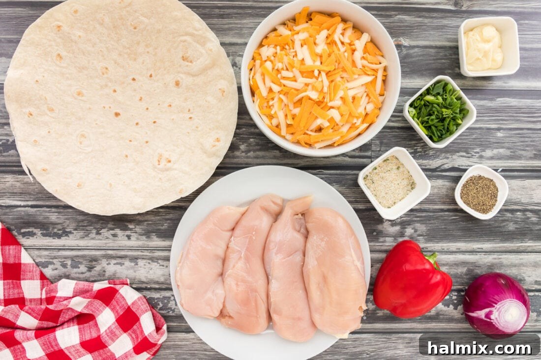 A collection of fresh ingredients laid out for making chicken quesadillas, including chicken breasts, cheeses, bell peppers, and onions