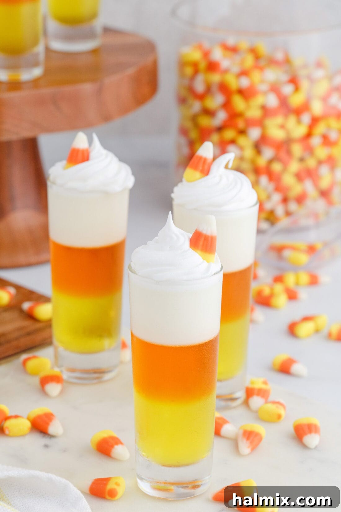 Close-up of a beautifully garnished Candy Corn Jello Shot with whipped cream and a small candy corn, ready to be enjoyed.