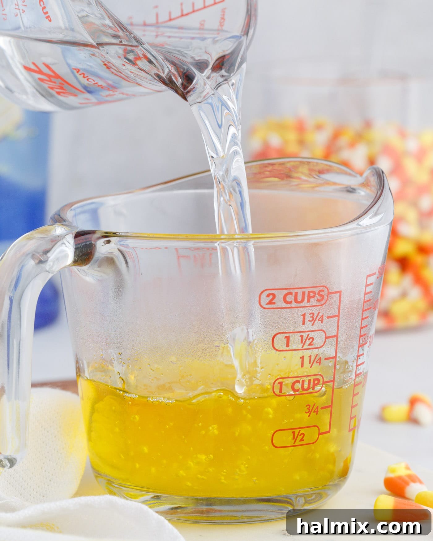 Pouring hot water into lemon jello mix in a spouted measuring cup, preparing the first layer for candy corn jello shots.