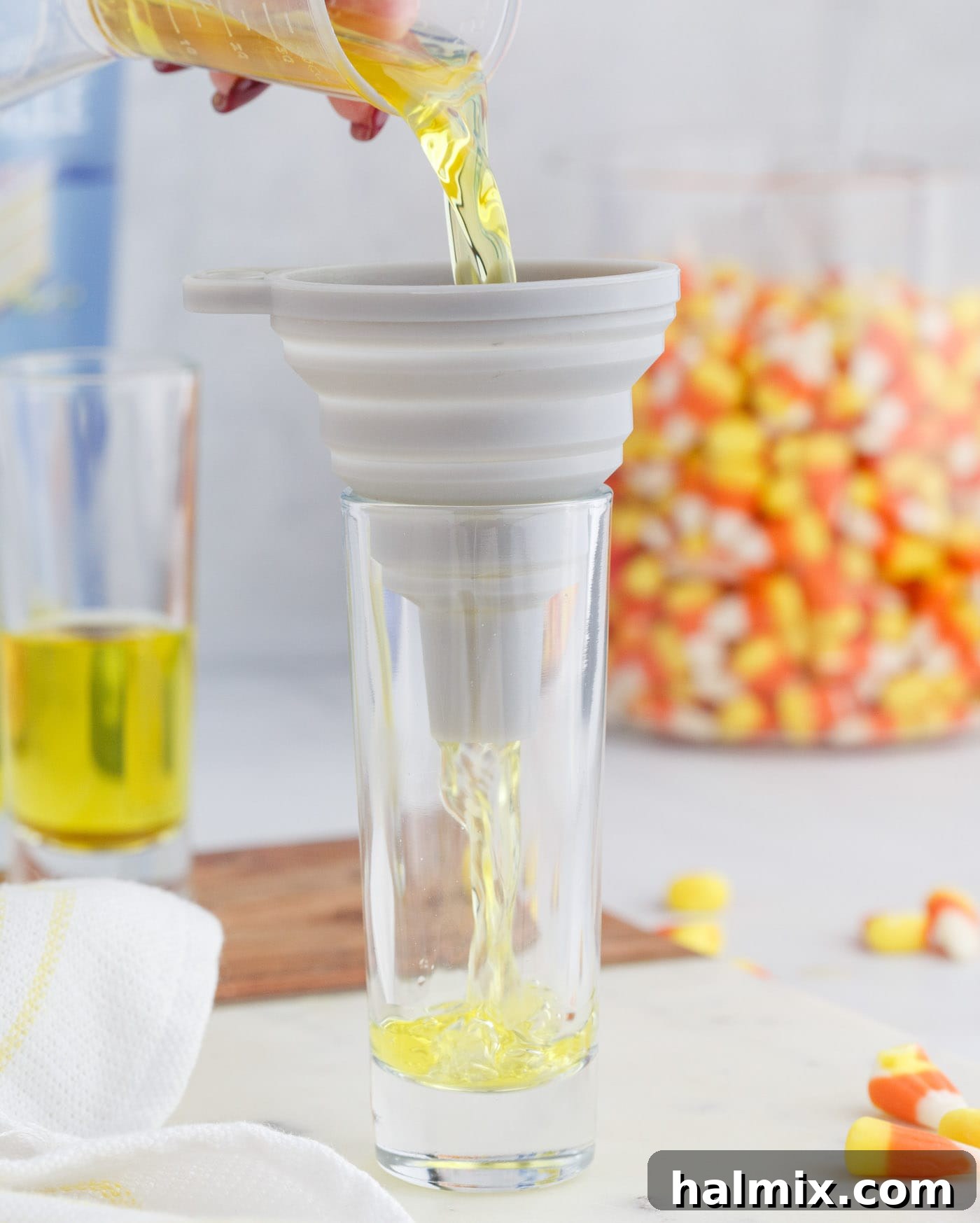 Carefully pouring the yellow lemon jello mixture into a shot glass, forming the base layer of a candy corn jello shot.