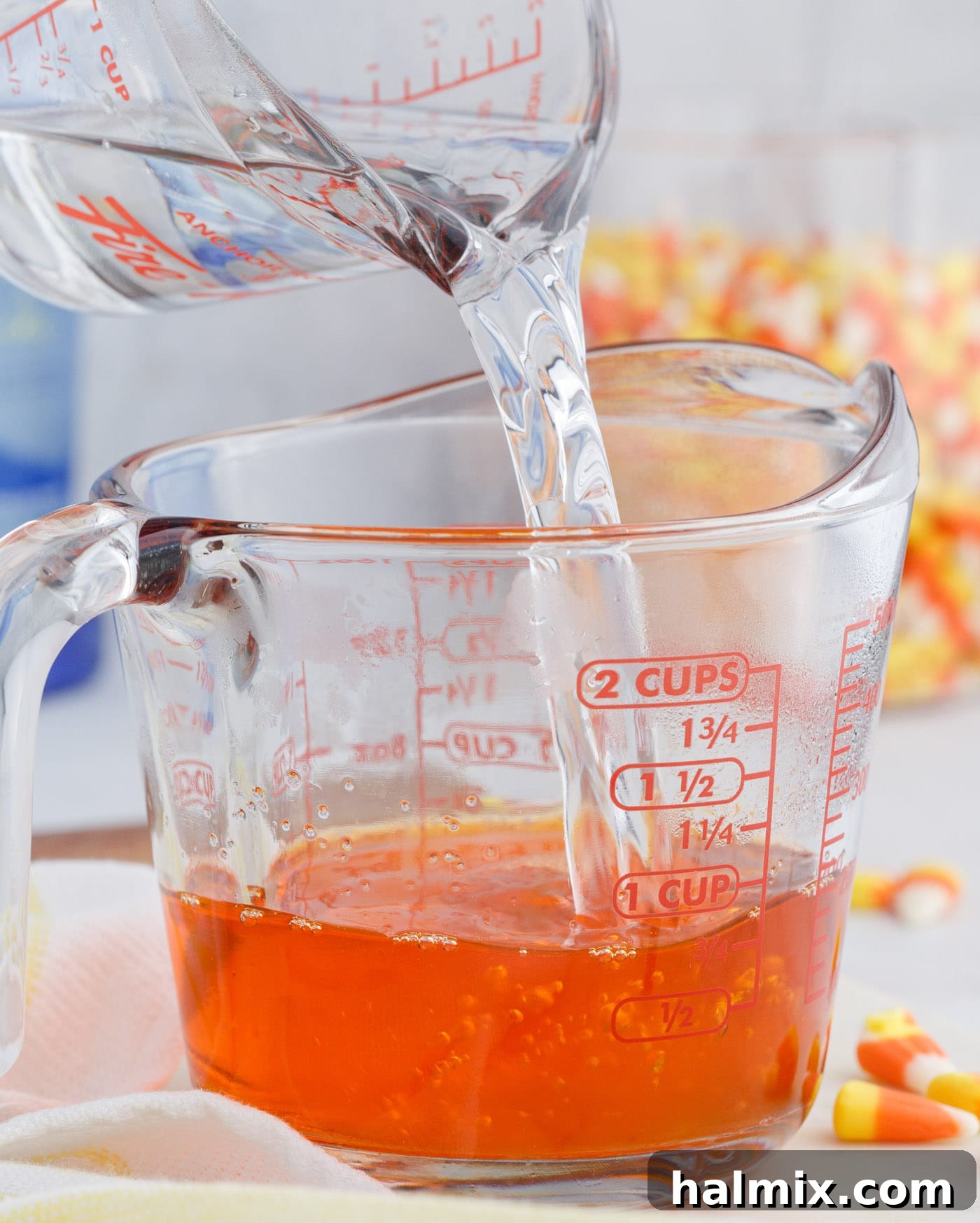 Adding hot water to orange jello mix in a measuring cup, preparing the vibrant orange layer for the jello shots.