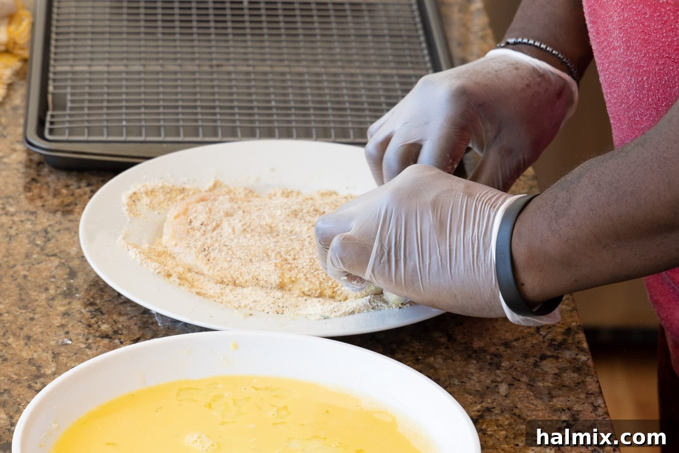 A chicken cutlet being pressed into the seasoned breadcrumb mixture