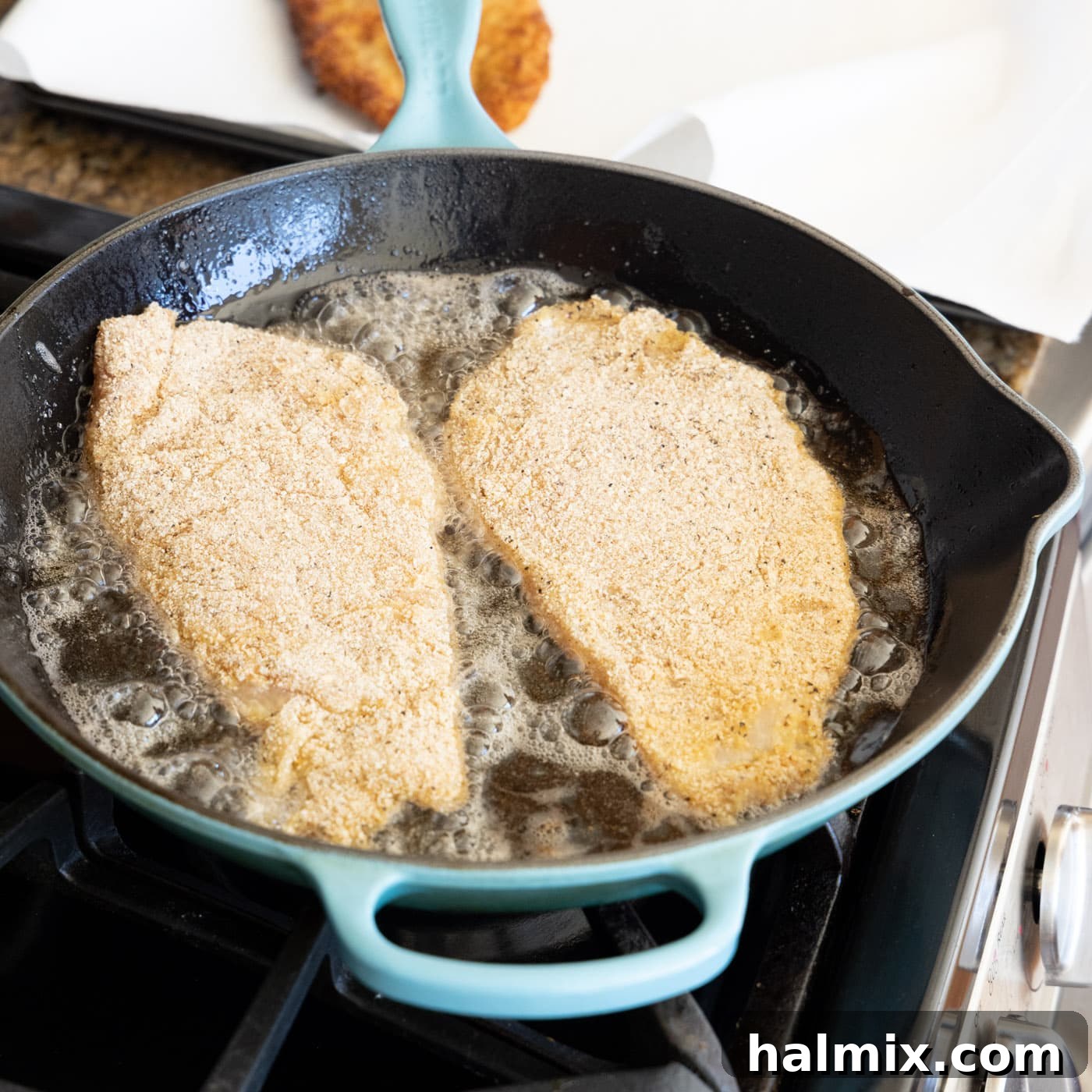 Crispy Golden Milanese Chicken 12 Two chicken cutlets sizzling in hot olive oil in a skillet, turning golden brown