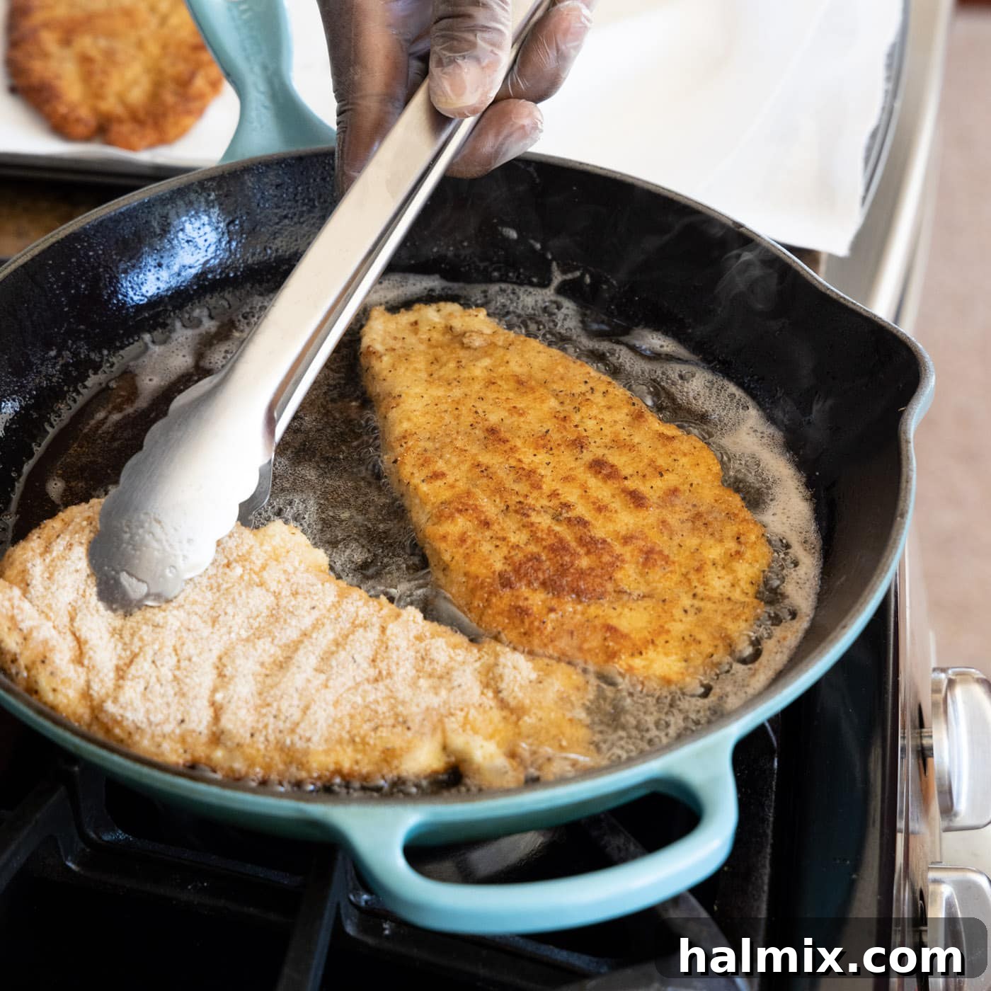 Tongs flipping a chicken cutlet in a skillet, revealing its golden-brown crispness