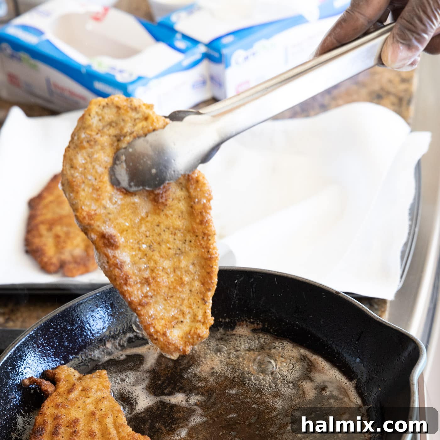 Freshly pan-fried Chicken Milanese cutlets being removed from the skillet and placed on paper towels