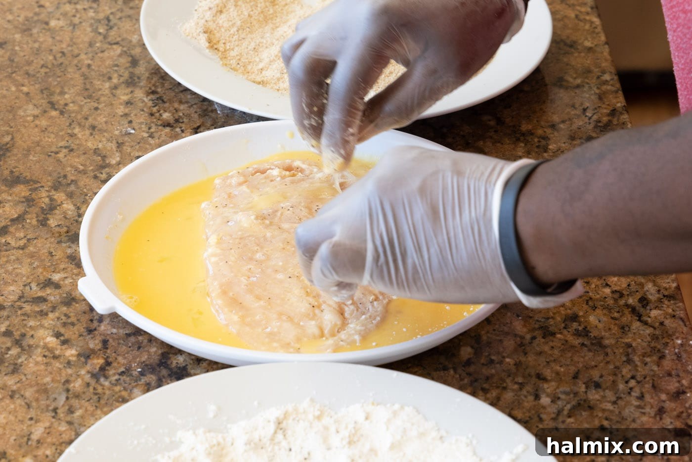 A floured chicken cutlet being dipped into the egg wash mixture