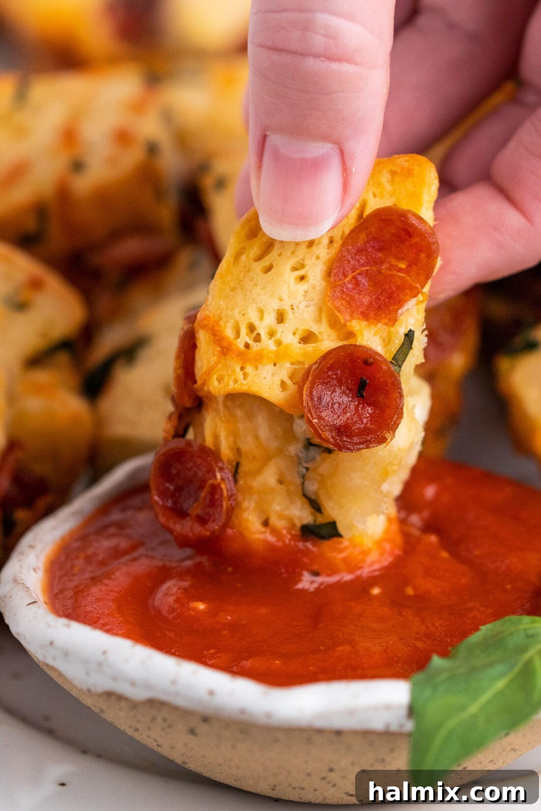 Pizza Zingers 12 A hand dipping a single pizza bite into a bowl of marinara sauce.