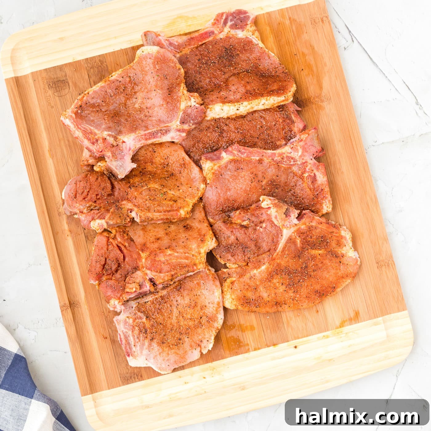 Pork chops being massaged with a savory oil and spice rub by gloved hands