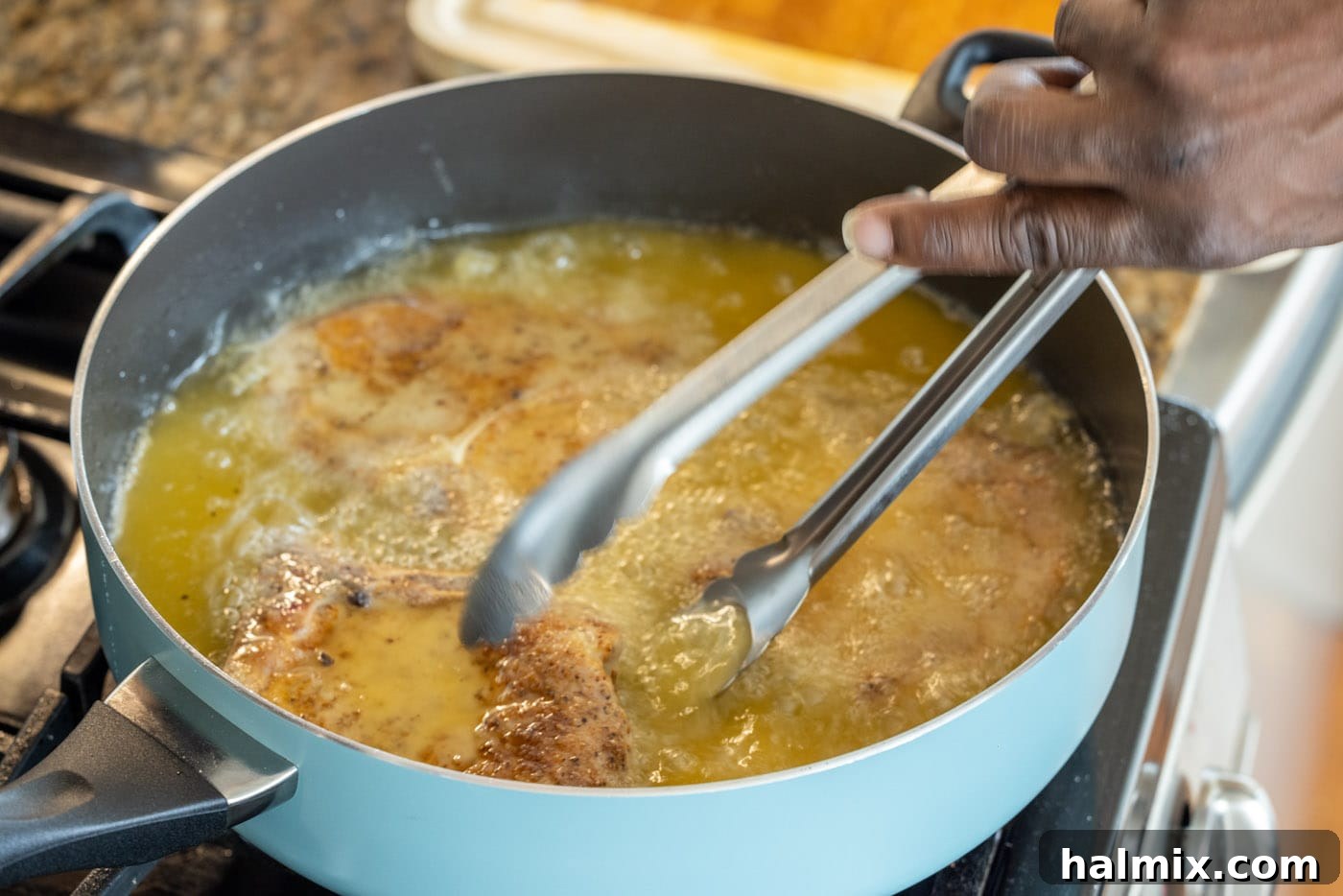 Tongs flipping a frying pork chop in a hot skillet, revealing a perfectly browned side