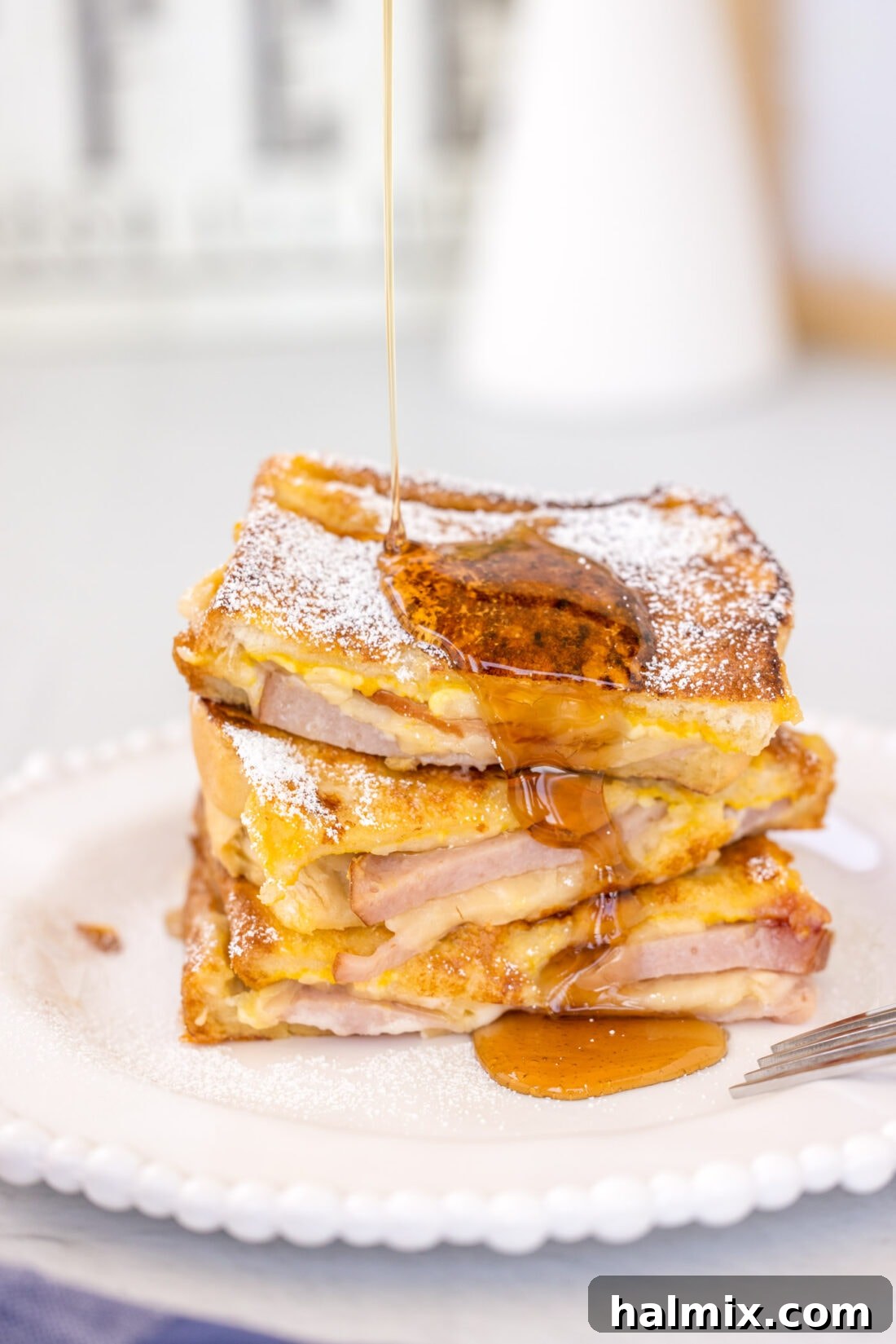 A delectable stack of Monte Cristo Sandwiches, lightly dusted with powdered sugar, ready to be enjoyed. Served with a side of sweet syrup.