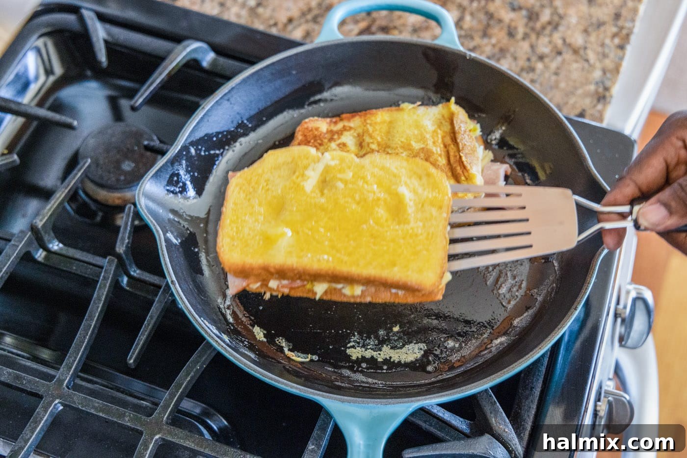 A spatula carefully flipping a Monte Cristo sandwich in a skillet to cook the other side.