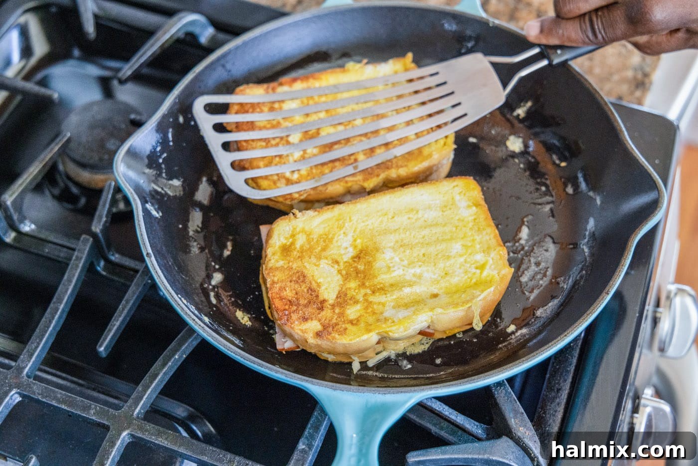 A close-up view of a Monte Cristo sandwich cooking in a hot skillet, showcasing the browning process.