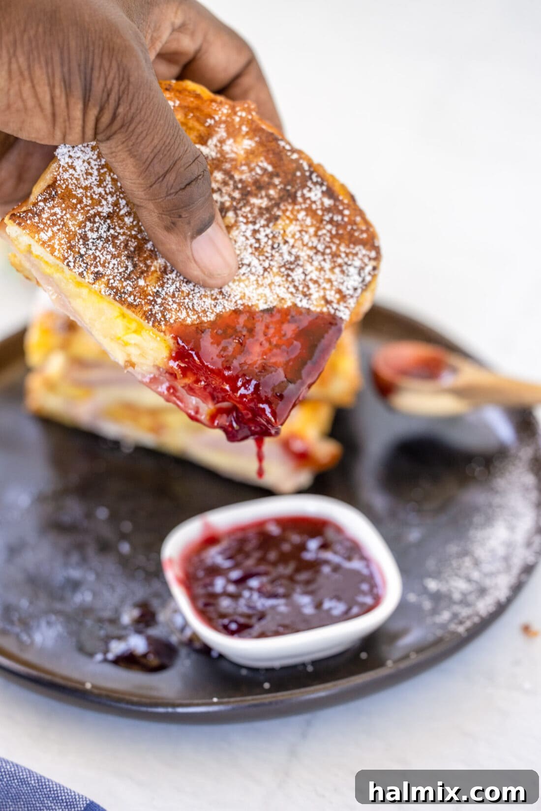 A Monte Cristo Sandwich being dipped into a small bowl of vibrant red raspberry jelly, showcasing the delicious pairing.