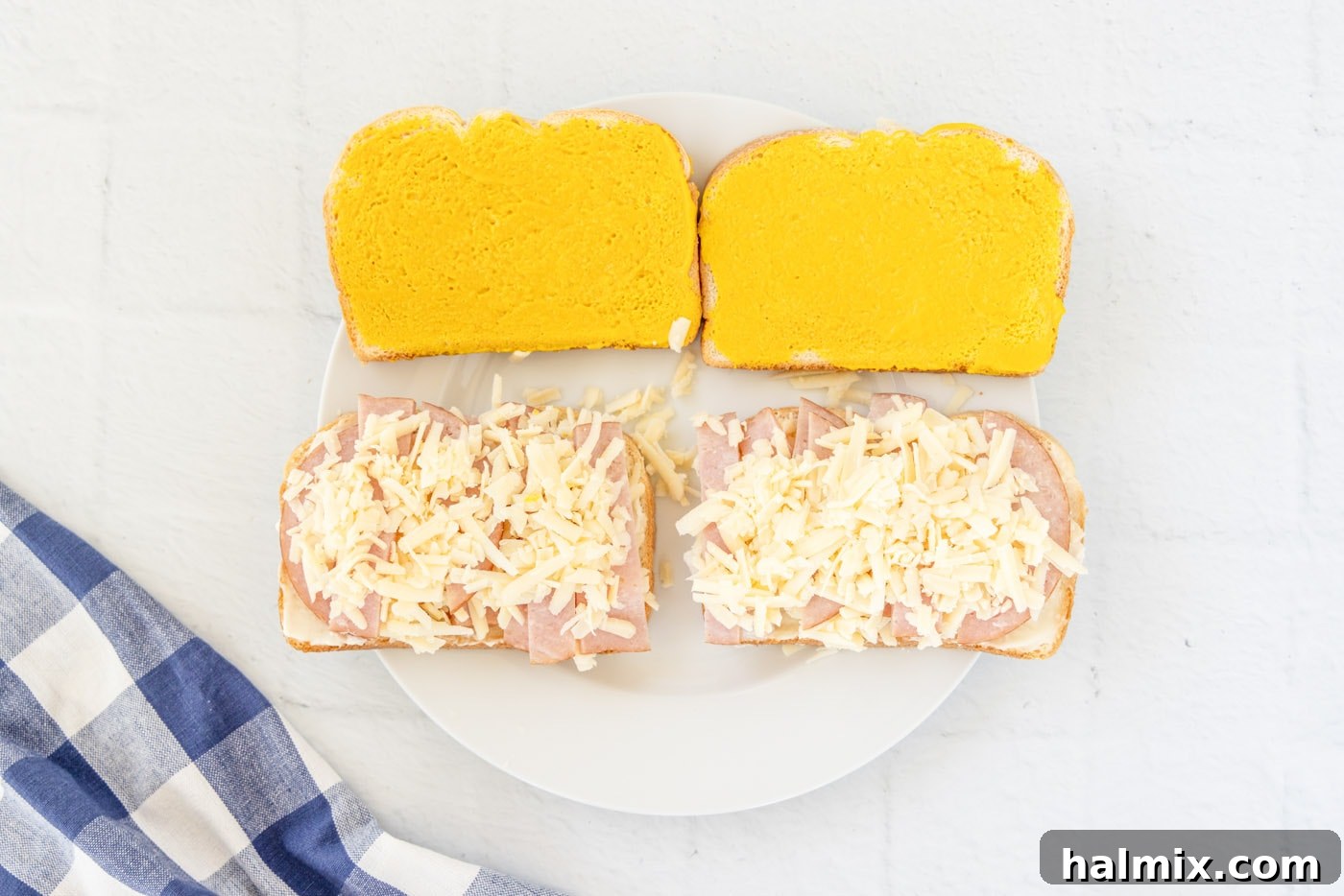 Shredded Gruyere cheese layered on top of mayonnaise and ham on a slice of bread, ready for the top slice.