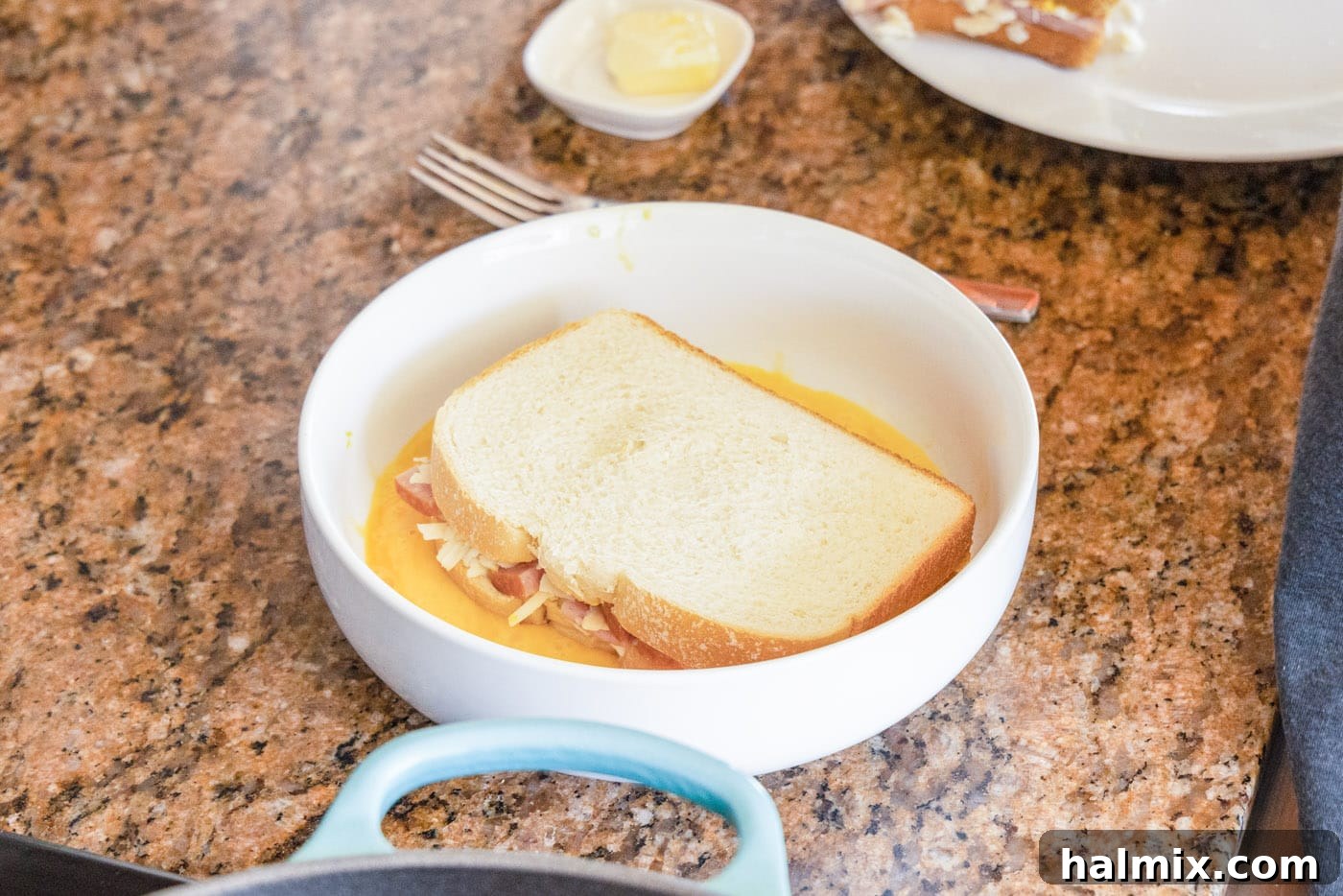 A Monte Cristo sandwich being carefully dredged in whisked egg batter, ensuring full coverage.