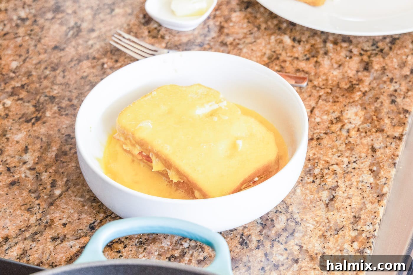An assembled Monte Cristo sandwich fully coated in whisked egg, ready for the skillet.