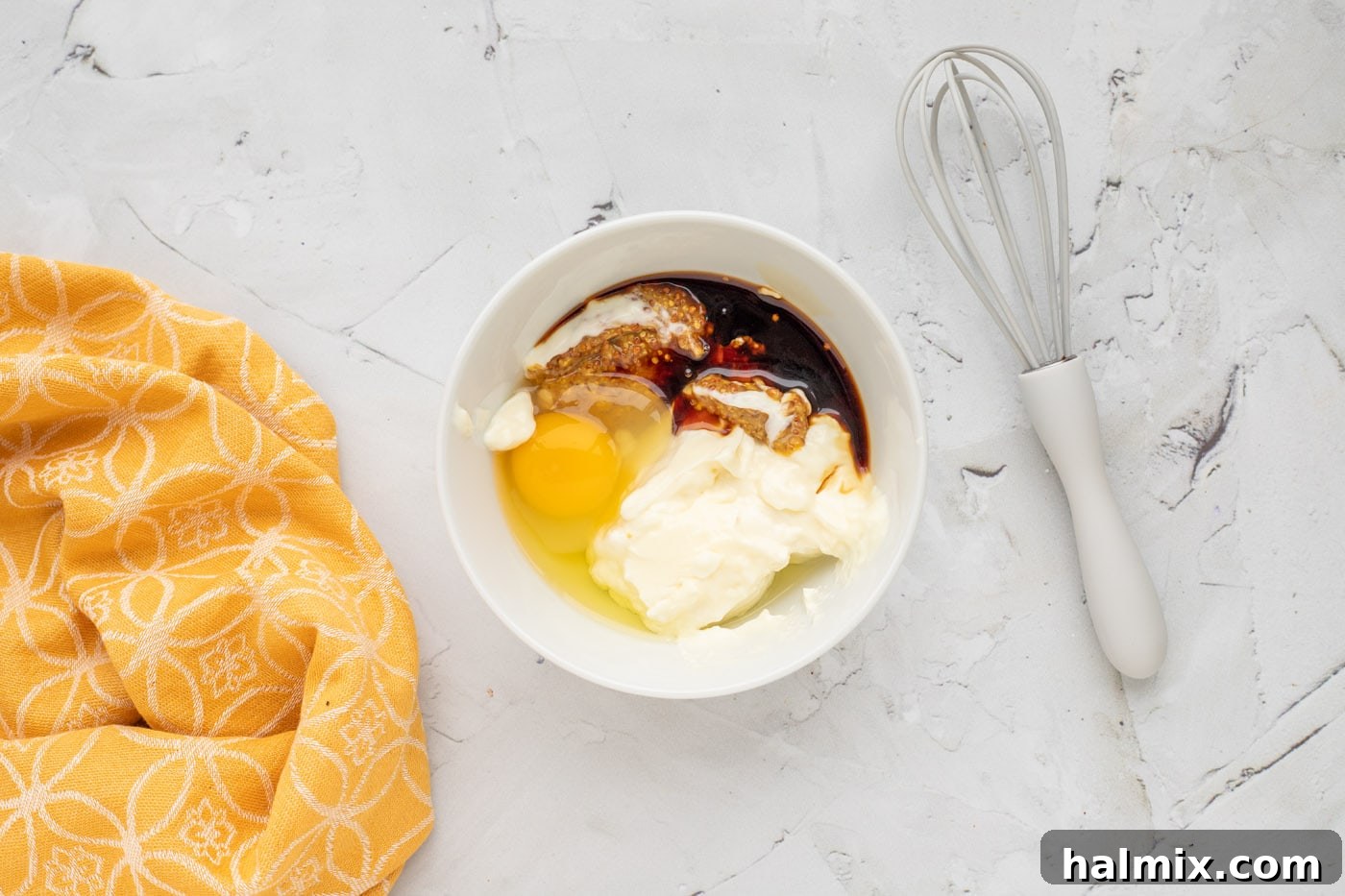 A bowl containing a whisked mixture of mayonnaise, soy sauce, ground mustard, egg, and horseradish mayo, ready for the next step.