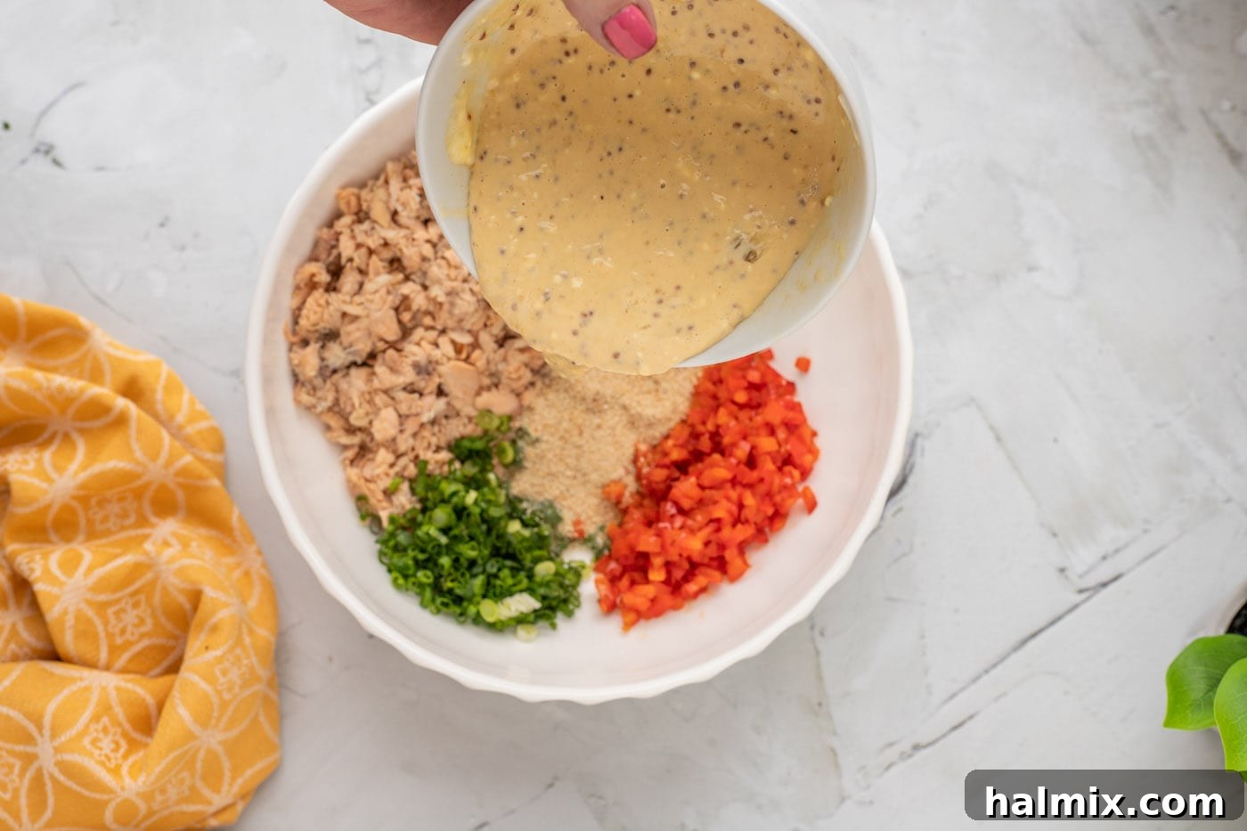 The mayonnaise mixture being poured over the salmon and breadcrumb mixture in a bowl, illustrating the combining step.