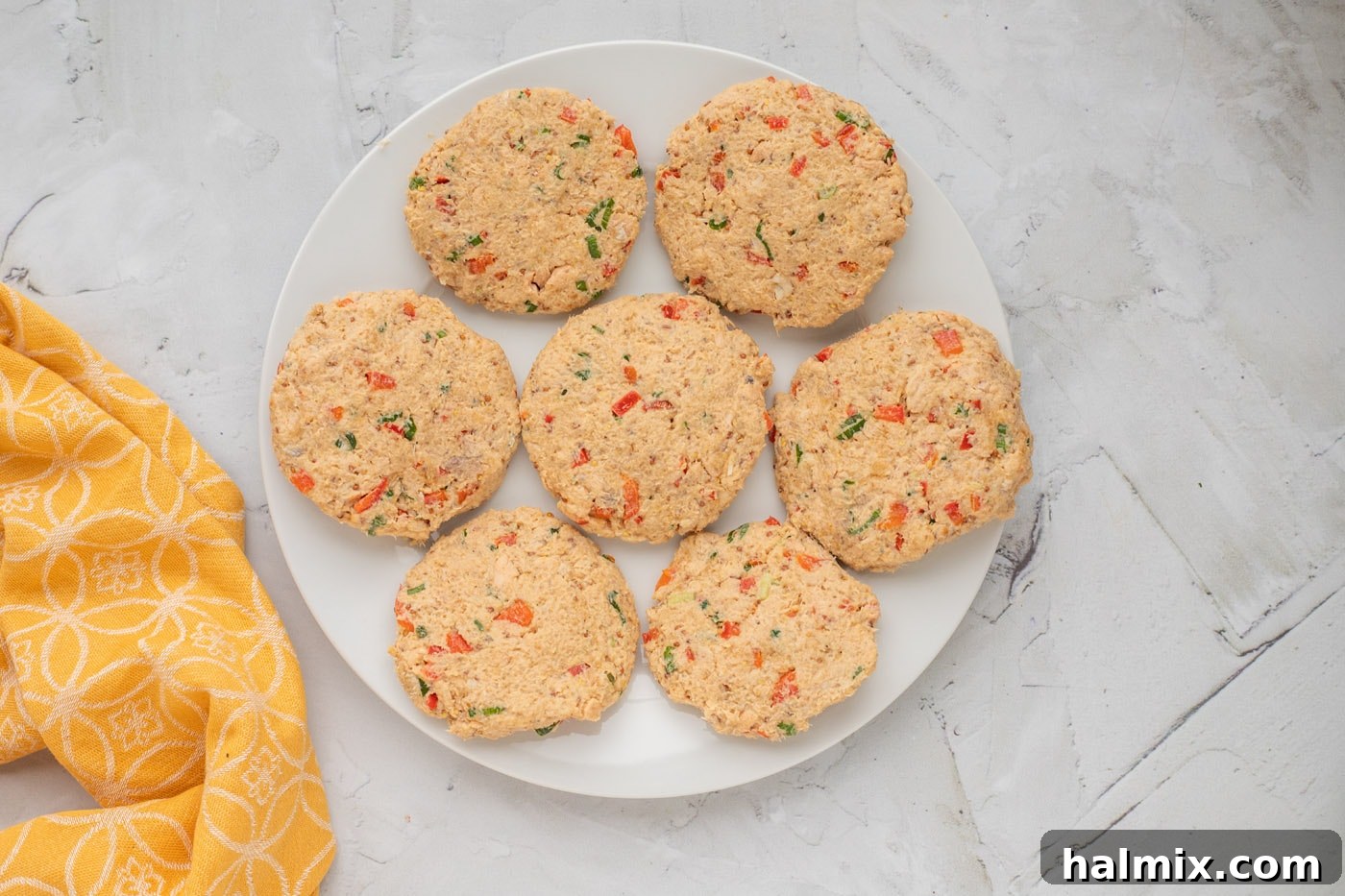 Seven perfectly formed salmon cakes arranged on a plate, ready for pan-frying.