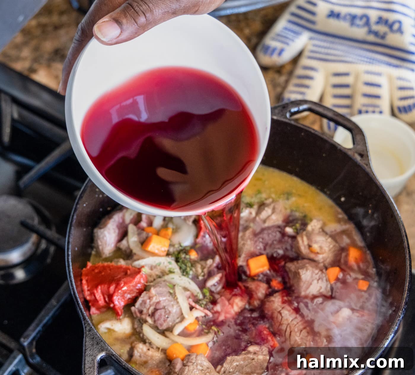 pouring rich red wine (Pinot Noir) into the dutch oven with beef, bacon, and vegetables for Beef Bourguignon