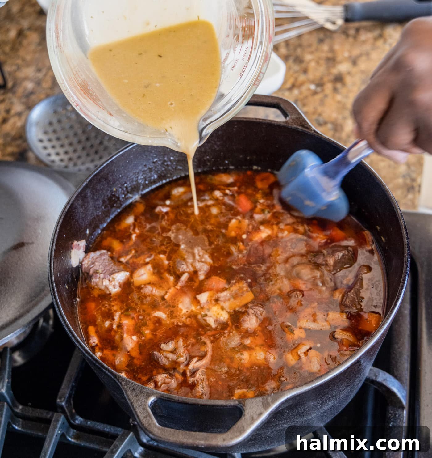 pouring the whisked flour and pan juice mixture back into the Beef Bourguignon in the dutch oven