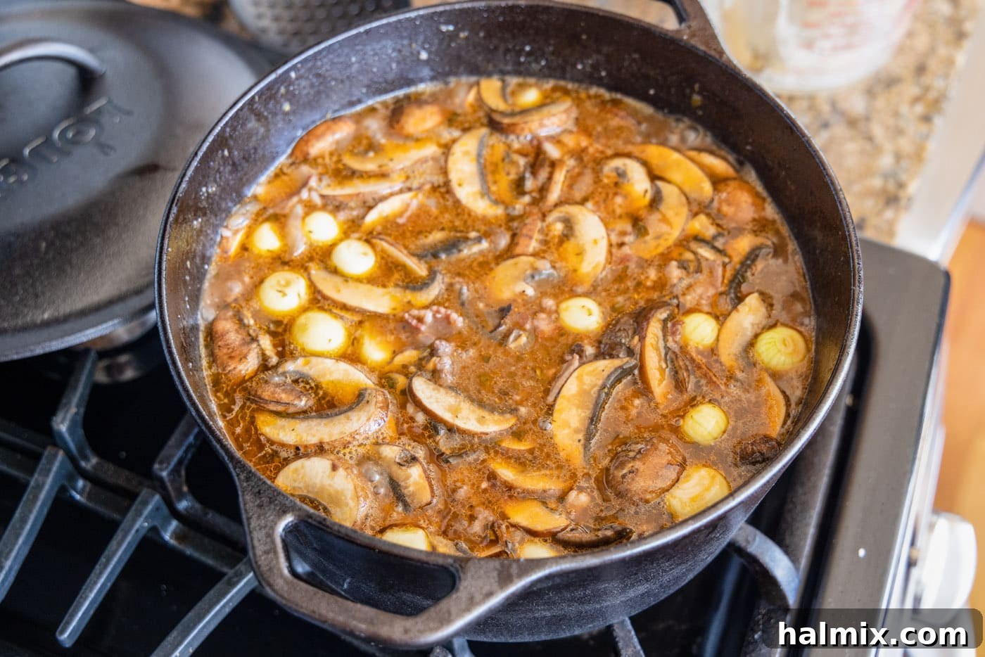 sliced baby bella mushrooms and pearl onions simmering in the Beef Bourguignon stew in a dutch oven