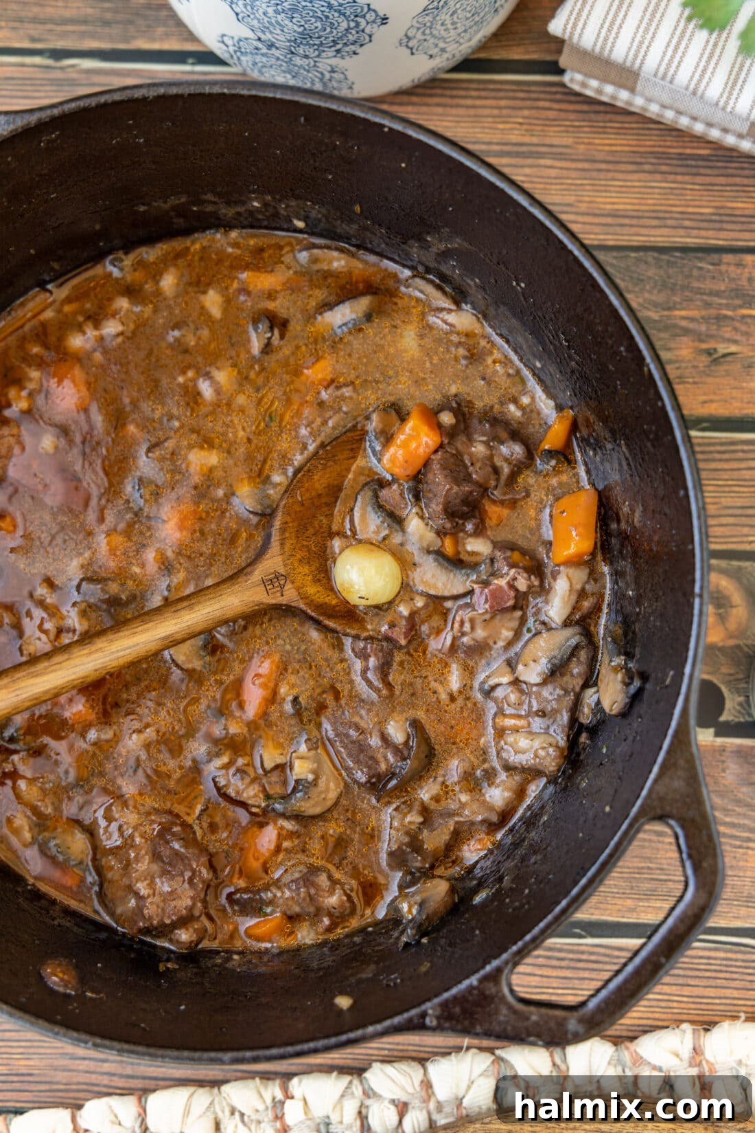 Beef Bourguignon in a cast iron pot with a wooden spoon, ready to be served, garnished with fresh herbs