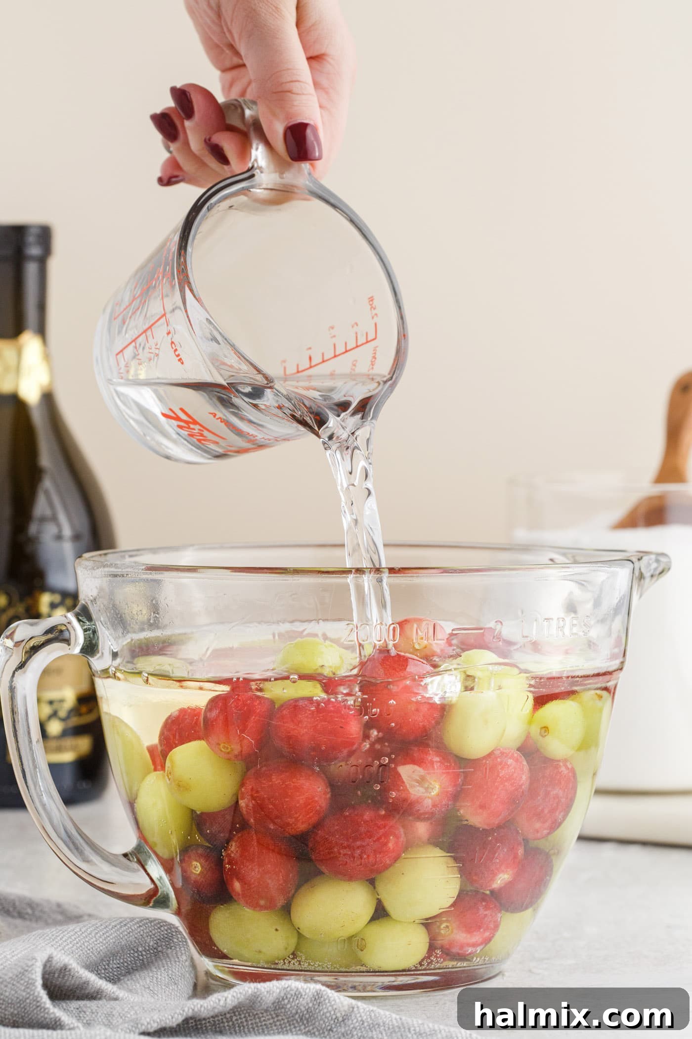 pouring vodka over prosecco and grapes in a bowl