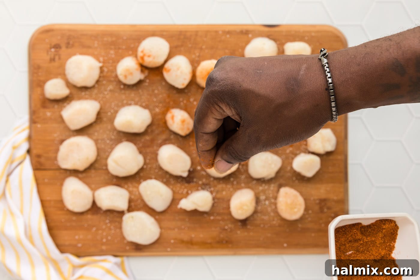 Seasoning scallops with Old Bay and garlic salt on a cutting board