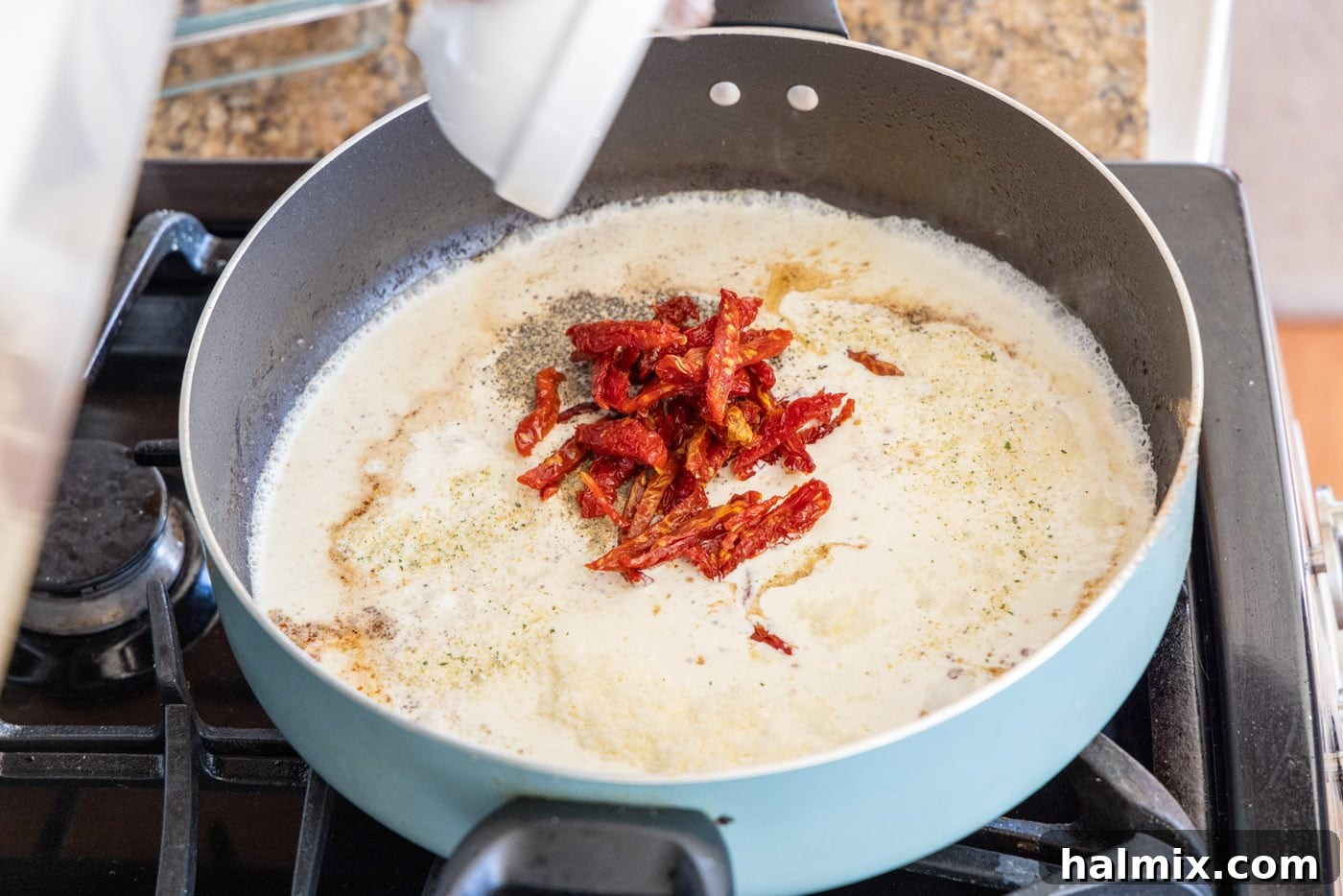 Adding sun dried tomatoes and other ingredients to the heavy cream mixture in the skillet.