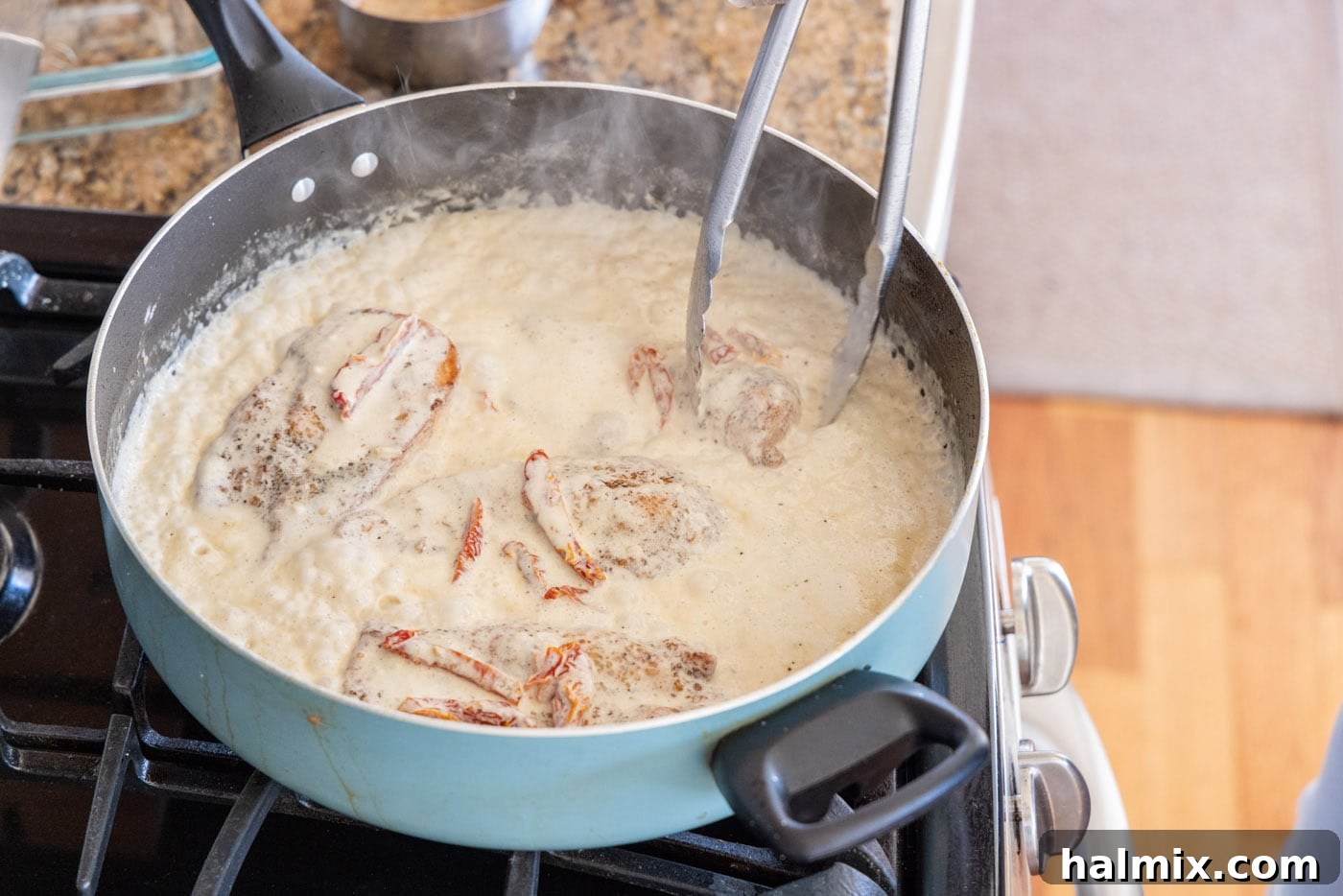 Flipping chicken breasts in a skillet with heavy cream sauce.