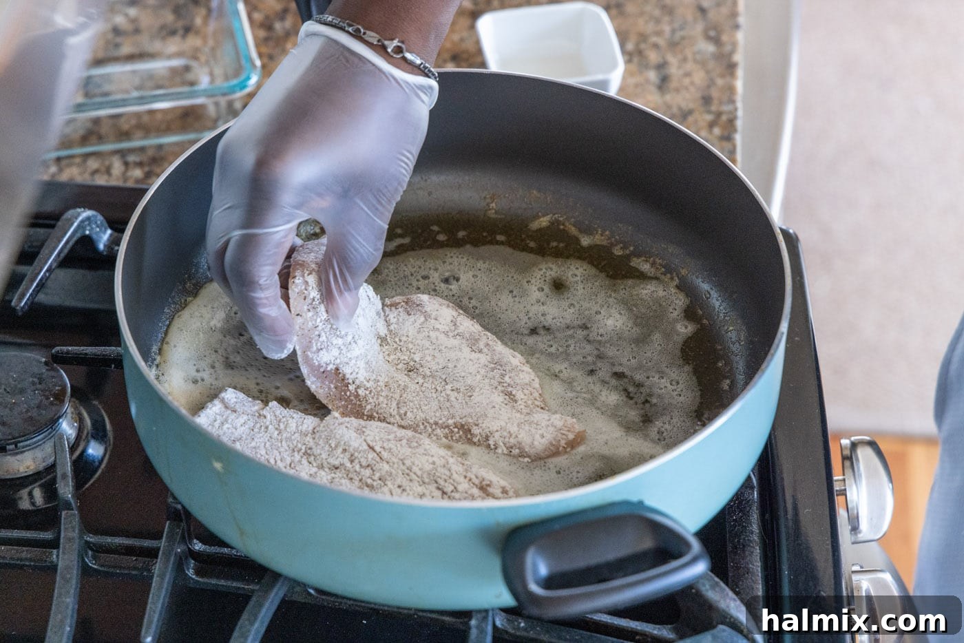 Adding floured chicken breast to the hot skillet.
