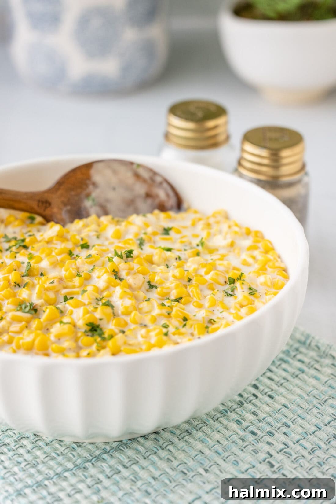 A large serving bowl filled with creamy homemade creamed corn, garnished with fresh green herbs.